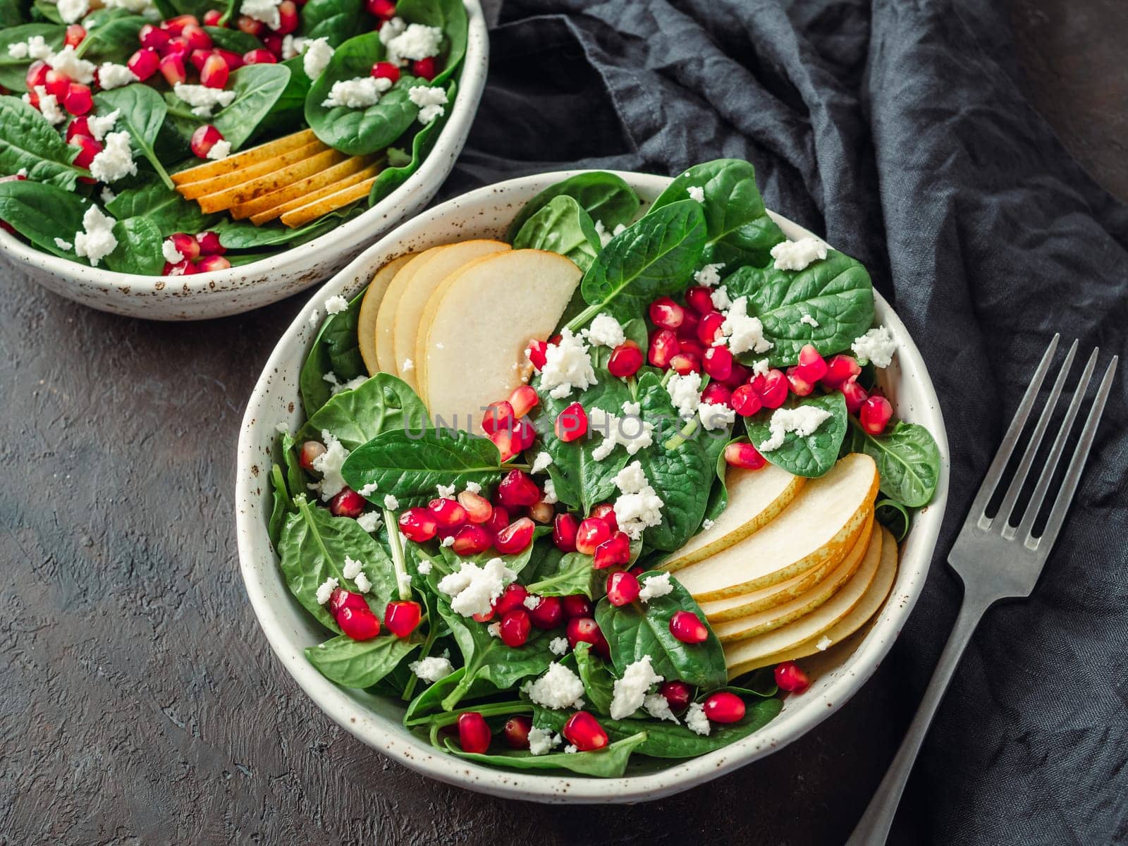 Vegan salad bowl with arugula, pear, pomegranate, cheese on black background. Vegan breakfast, vegetarian food, diet concept. Top view or flat lay. Copy space for text.