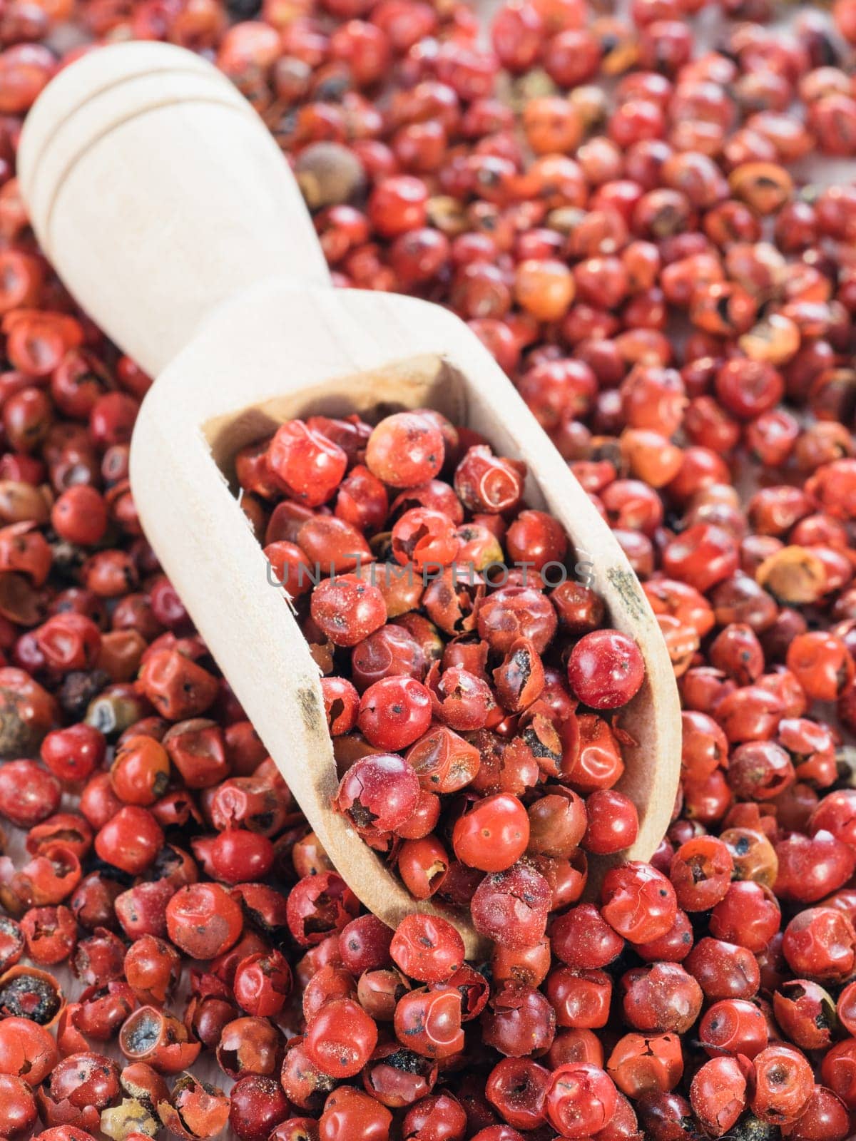 Wooden scoop filled with dried pink pepper berries. Close up view of pink peppercorn.