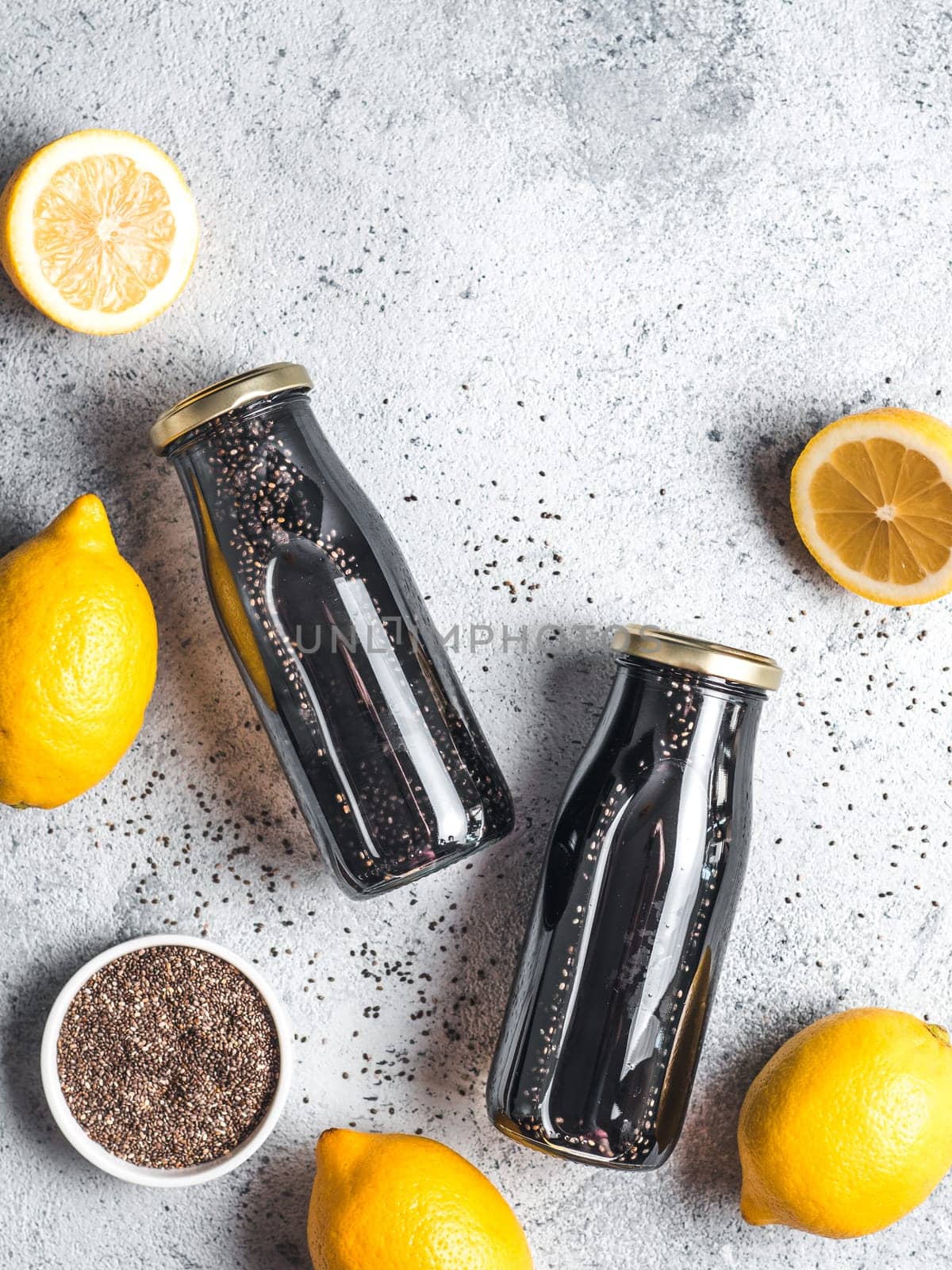 Detox activated charcoal black chia water or lemonade with lemon. Two bottle with black chia infused water. Detox drink idea and recipe. Vegan food and drink. Top view. Copy space for text. Vertical.