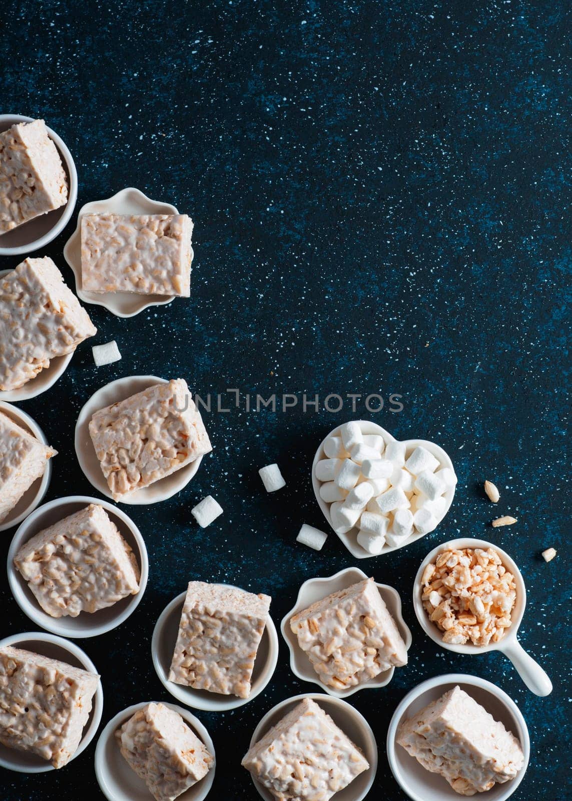 Homemade square bars of Marshmallow and crispy rice and ingredients on dark blue background. American dessert with marshmallow and crispy rice. Top view. Copy space