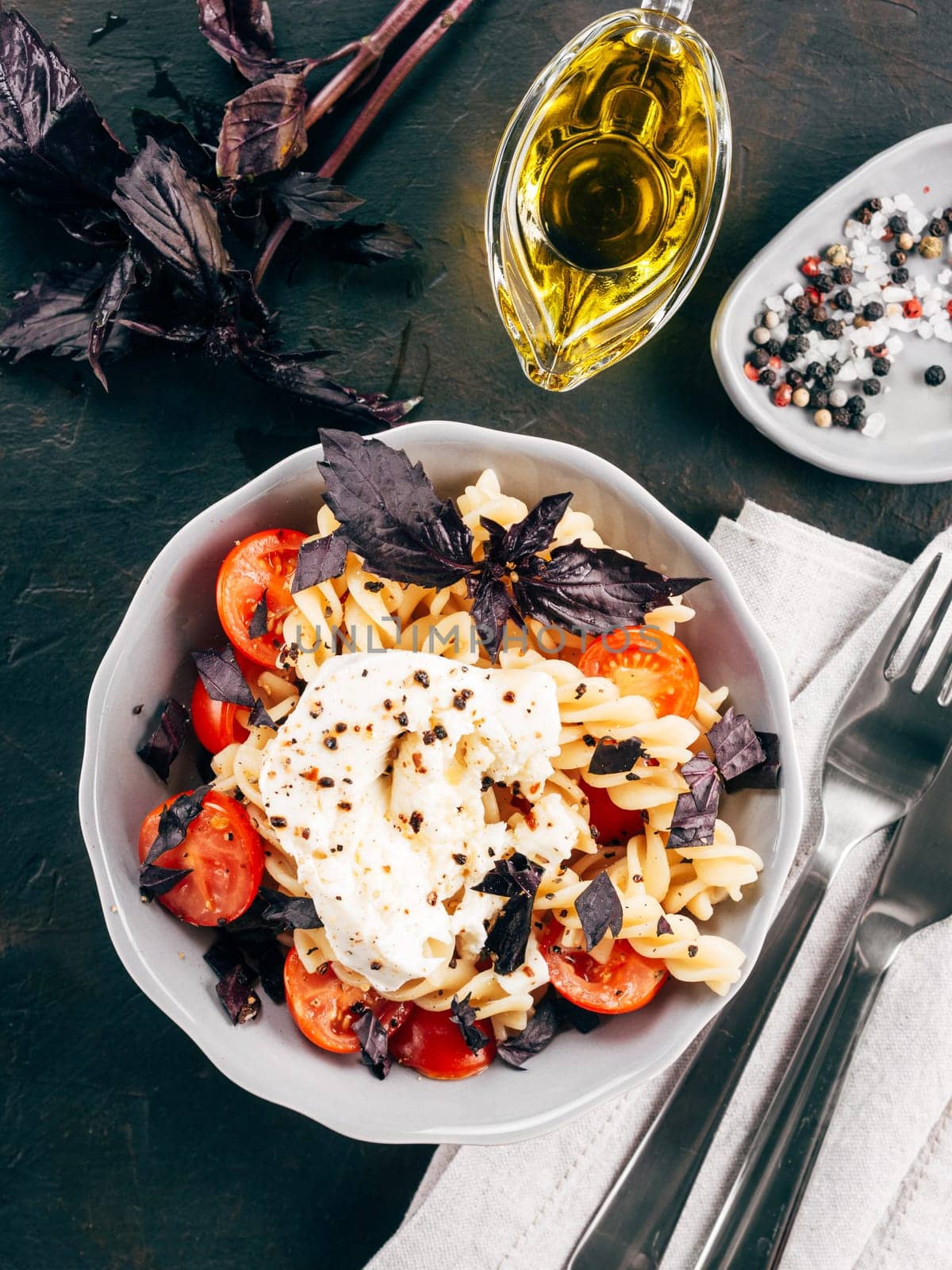 Tasty italian fusilli pasta with cherry, mozarella or buratta cheese and fresh basil. Dish with pasta on black concrete background. Top view. Copy space. Healthy food concept and recipe idea. Vertical