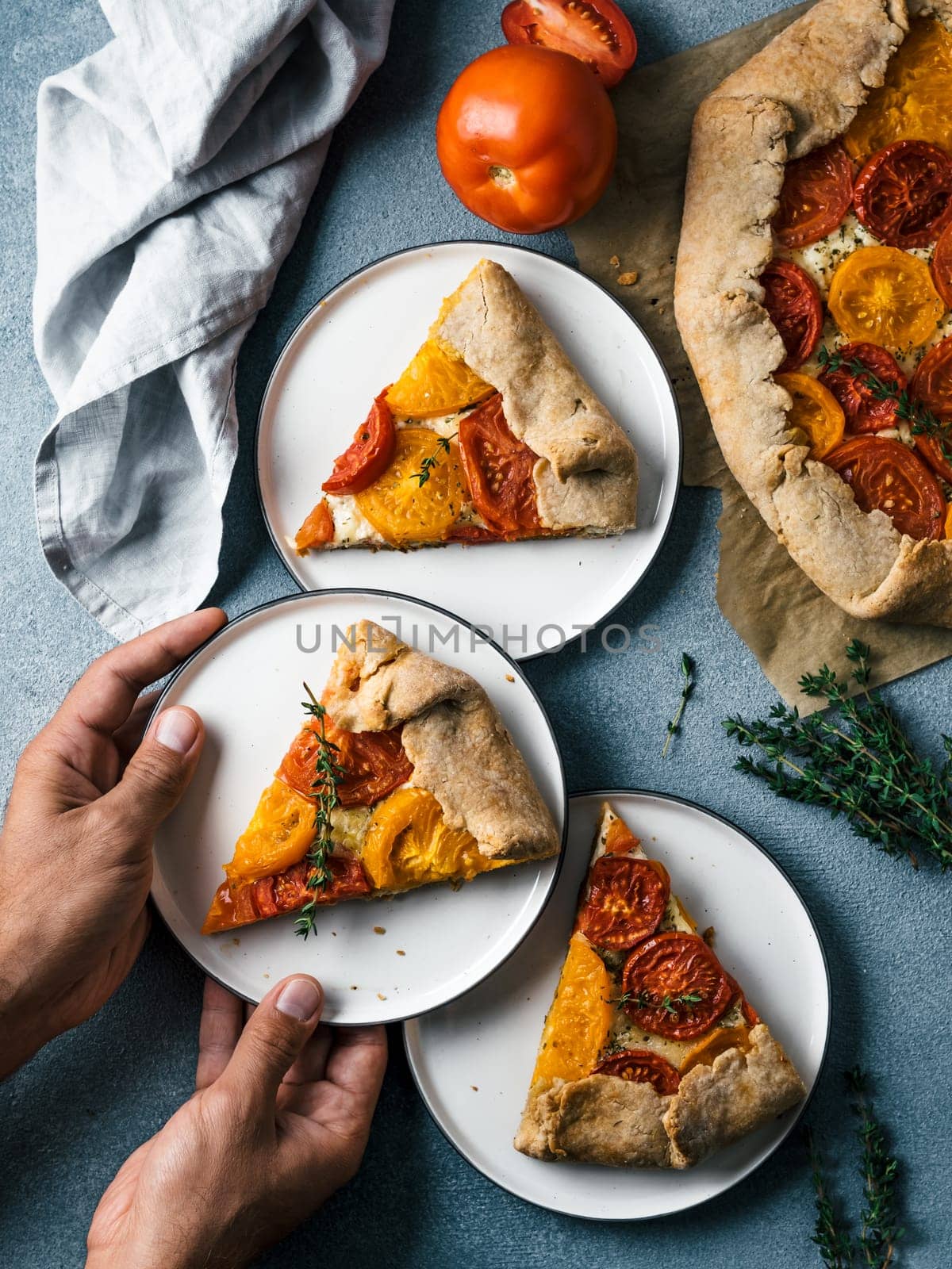 Savory fresh homemade tomato tart or galette.Hands takes piece of pie.Ideas and recipes healthy lunch,appetiezer-whole wheat or rye-wheat pie with tomatoes,cheese.Harvest tomatoes.Top view.Vertical