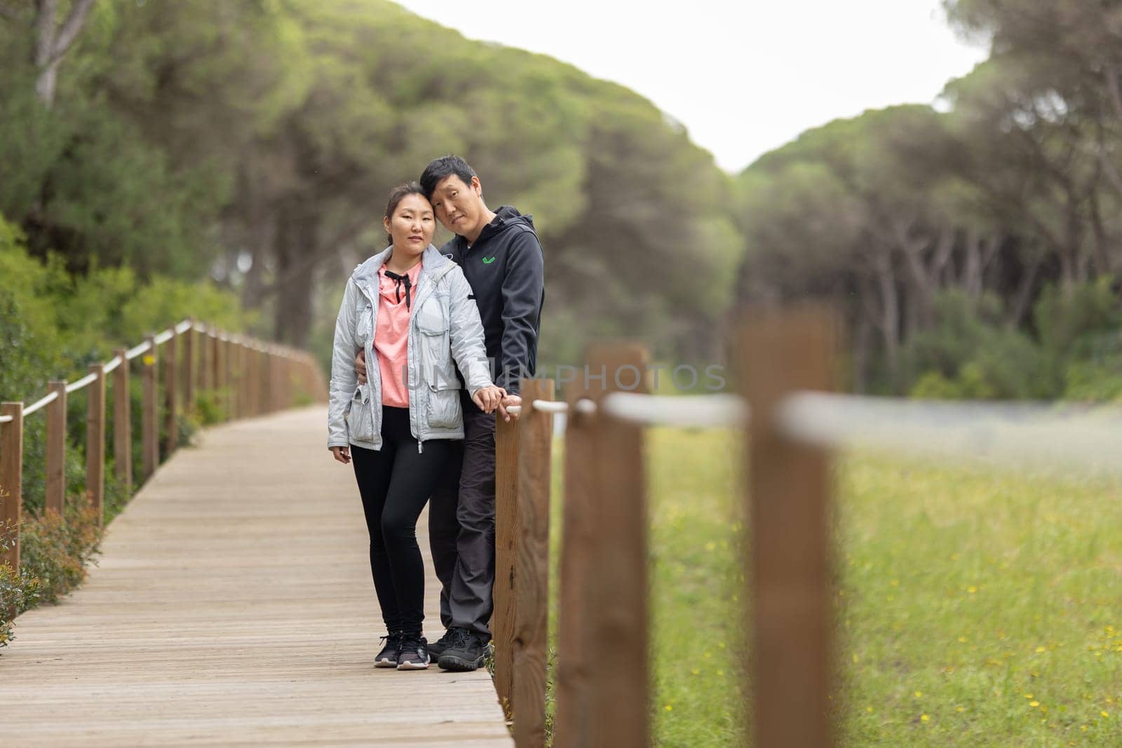 A couple standing on a wooden bridge, one of them wearing a pink shirt. Scene is romantic and peaceful