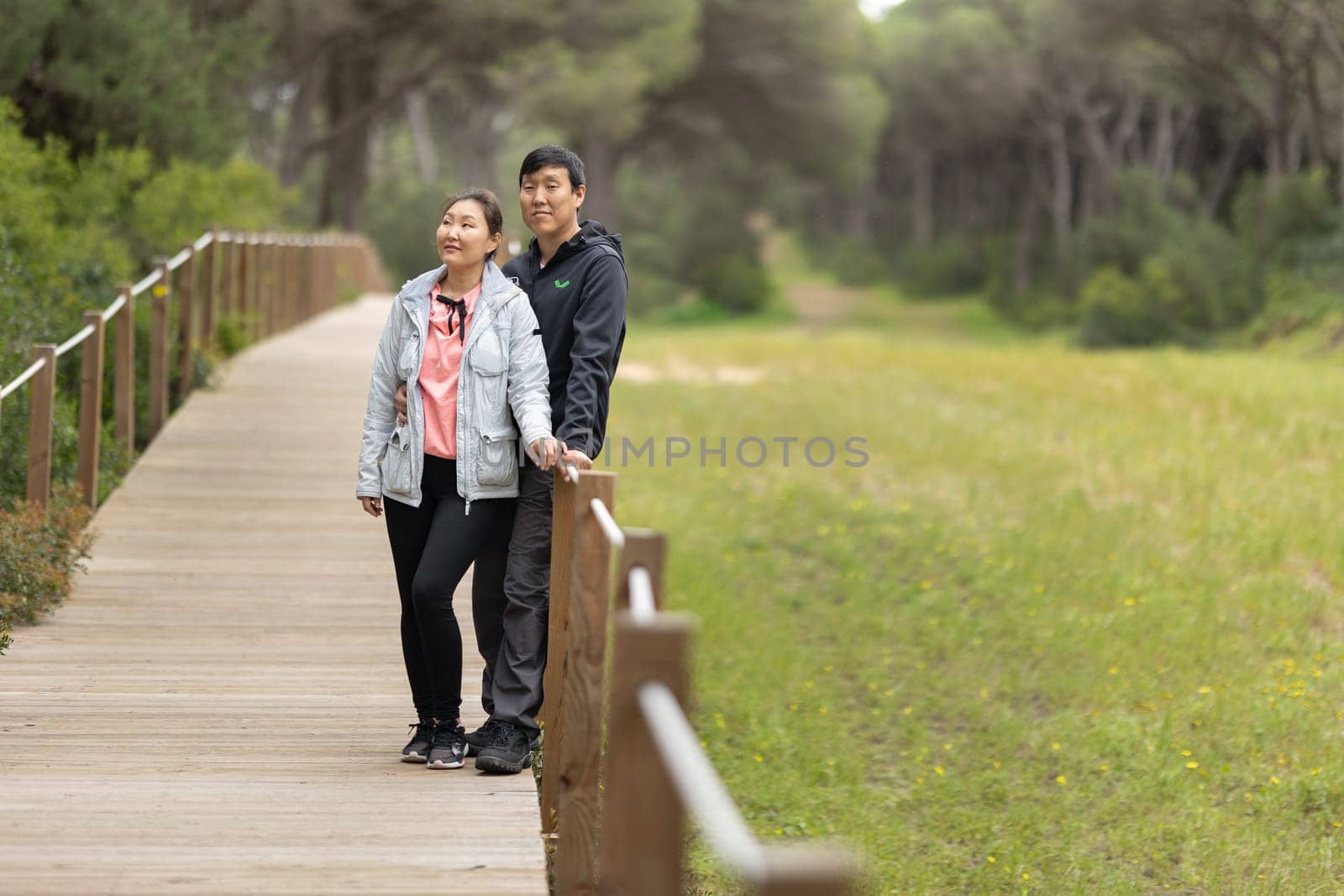 A couple standing on a wooden bridge, one of them wearing a black jacket. Scene is romantic and peaceful