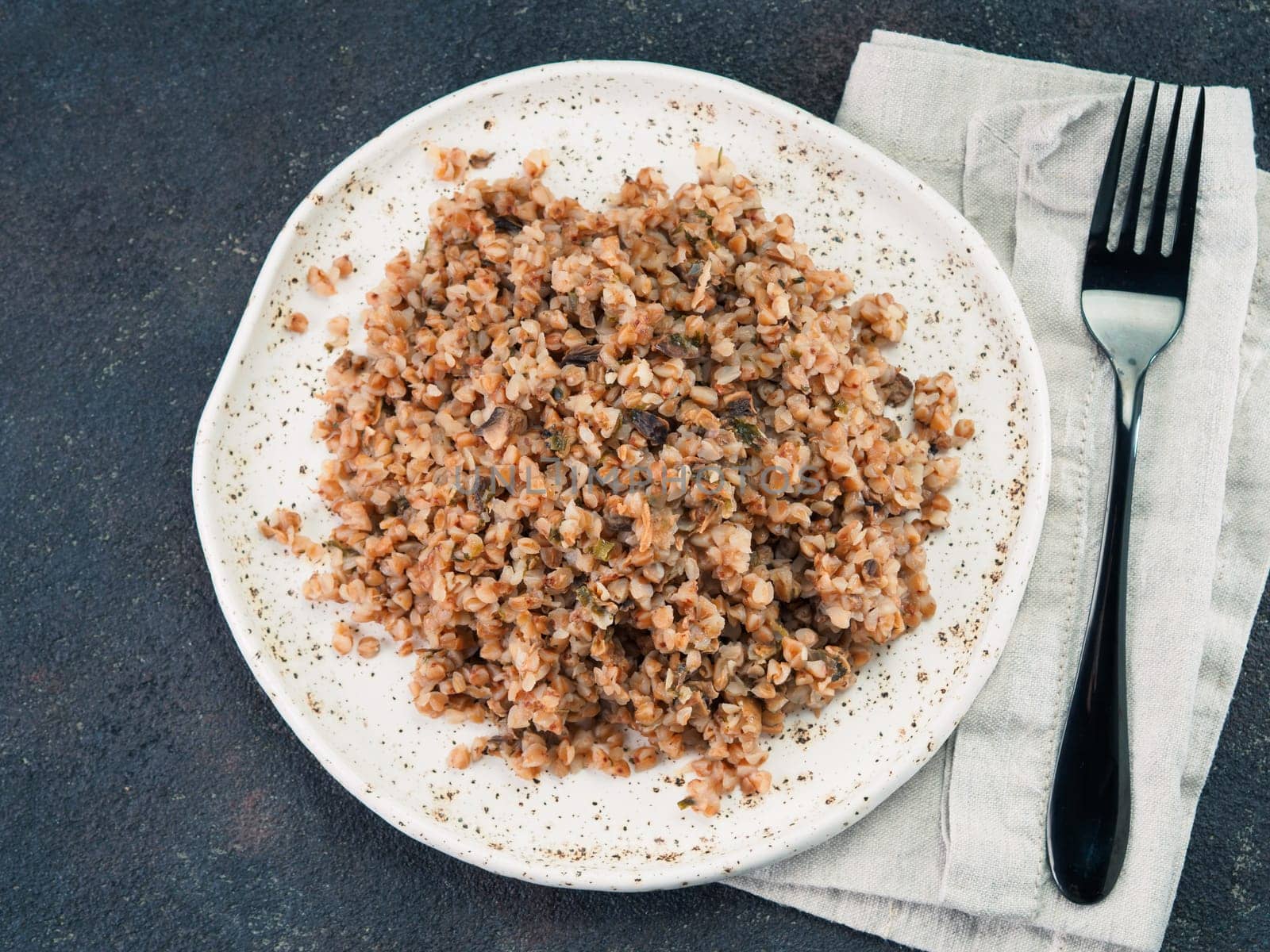 Buckwheat risotto with dried mushrooms in craft plate on black cement background. Gluten-free and vegetarian buckwheat recipe ideas. Copy space. Top view or flat-lay.