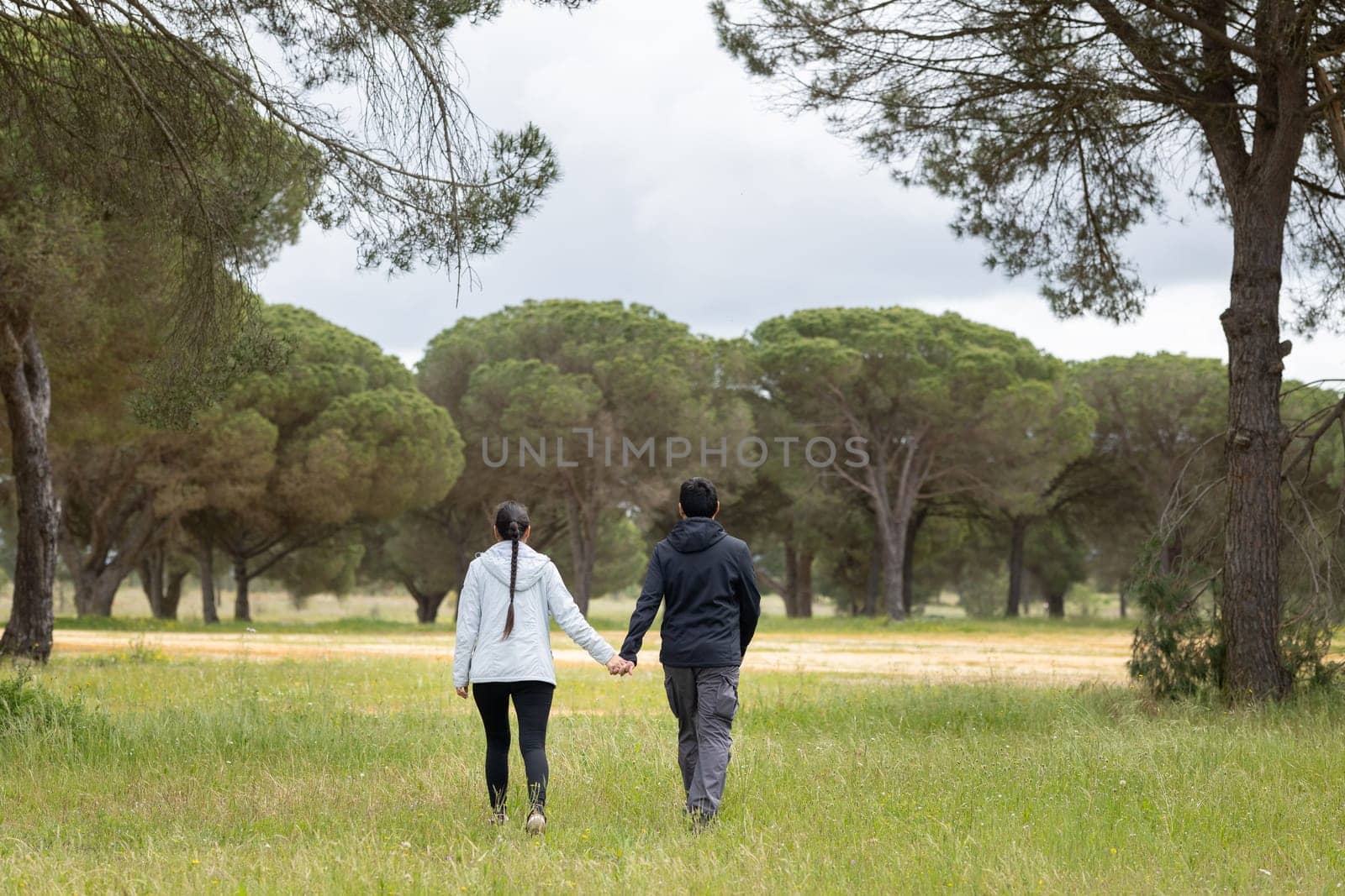 A couple is walking in a field with trees in the background. The man is wearing a black jacket and the woman is wearing a white jacket