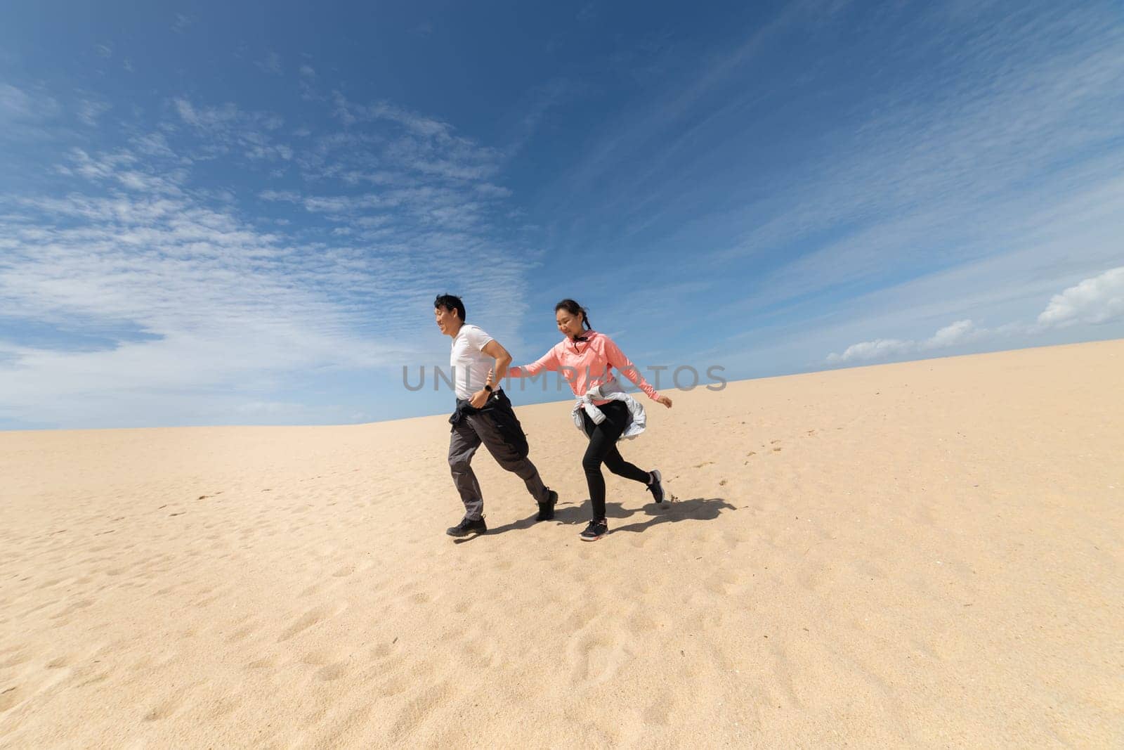 A man and woman are running on a sandy beach by Studia72