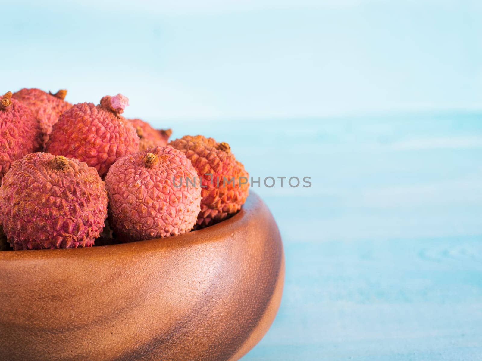 lychee fruit in clay plate on blue wooden background close up