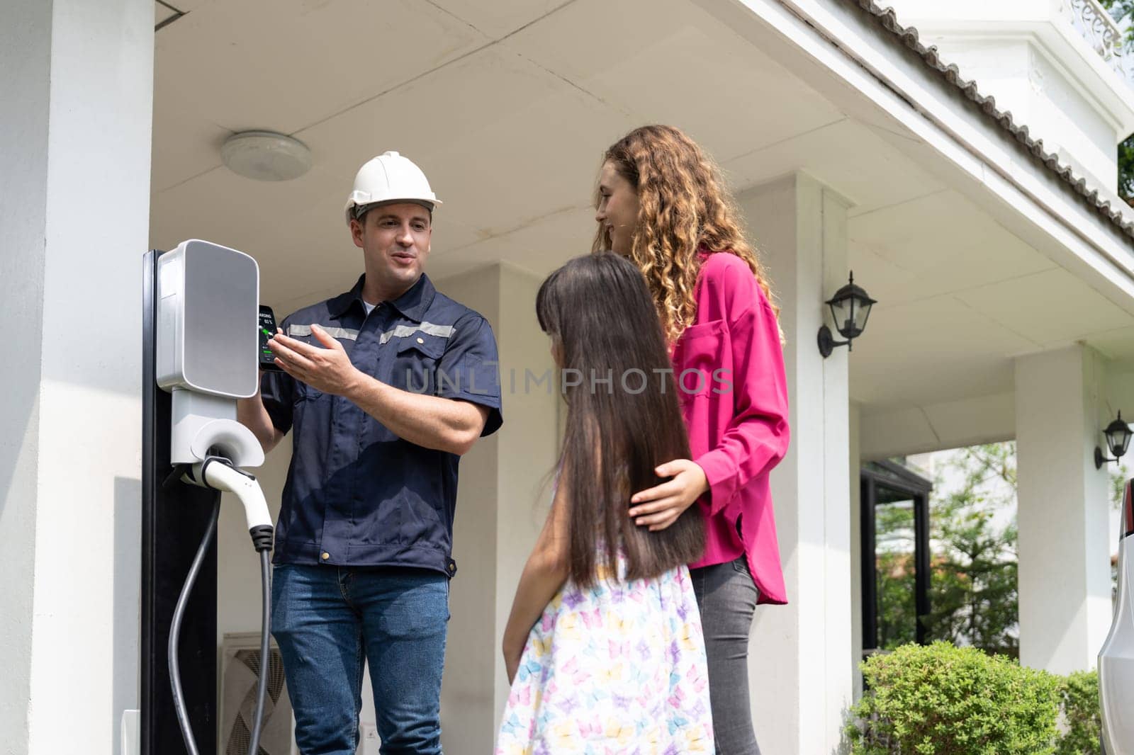 Technician install home EV charging station, providing service support for EV app on customer smartphone for monitoring charging status and set charging schedules at home. Synchronos