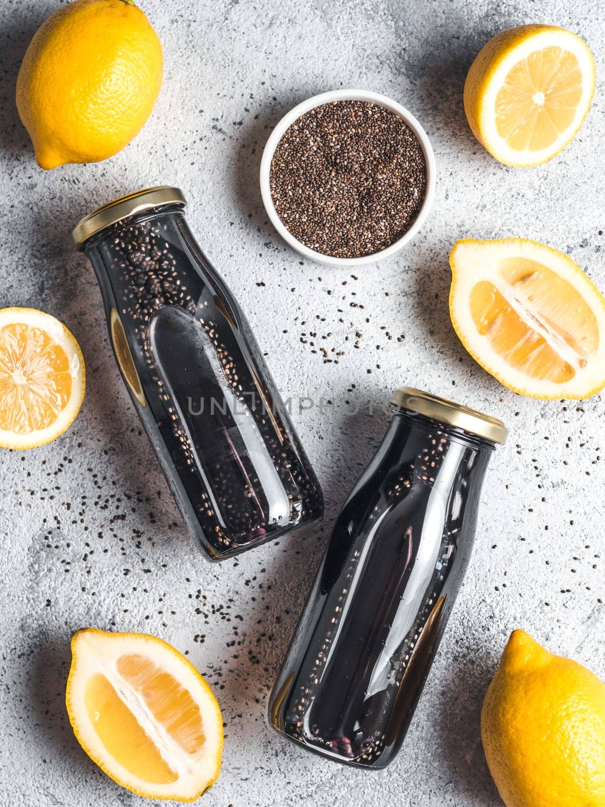 Detox activated charcoal black chia water or lemonade with lemon. Two bottle with black chia infused water. Detox drink idea and recipe. Vegan food and drink. Top view. Vertical.