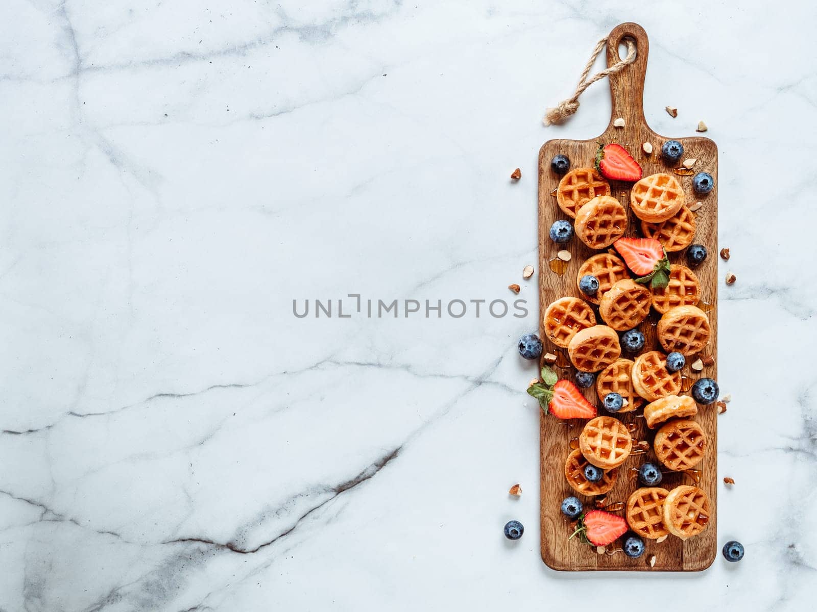 Small round delicious soft belgian waffles on cutting board. Fresh belgian waffles with berries and caramel sauce top view. Copy space for text or mock up