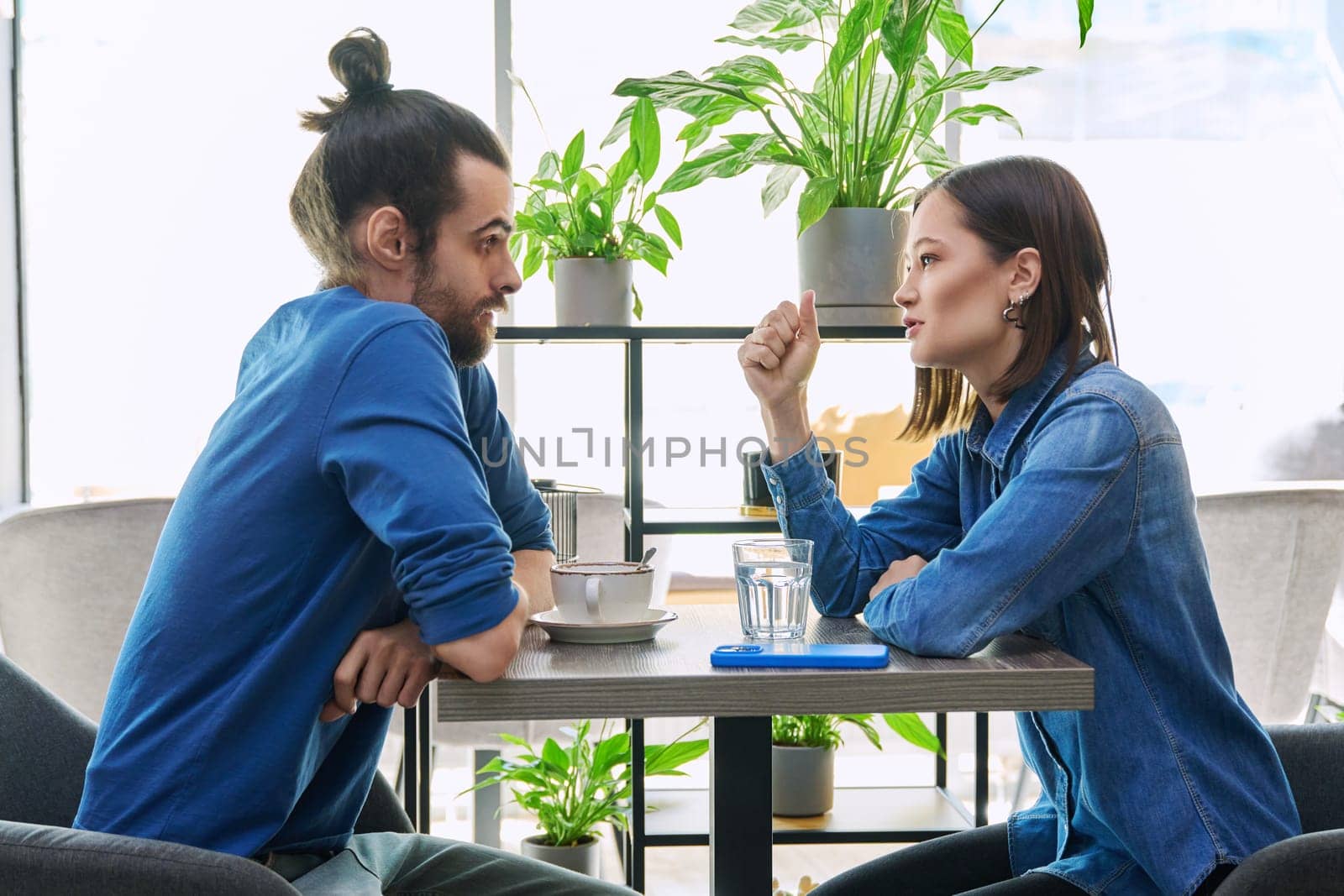 Young couple having serious conversation while sitting together in cafe by VH-studio