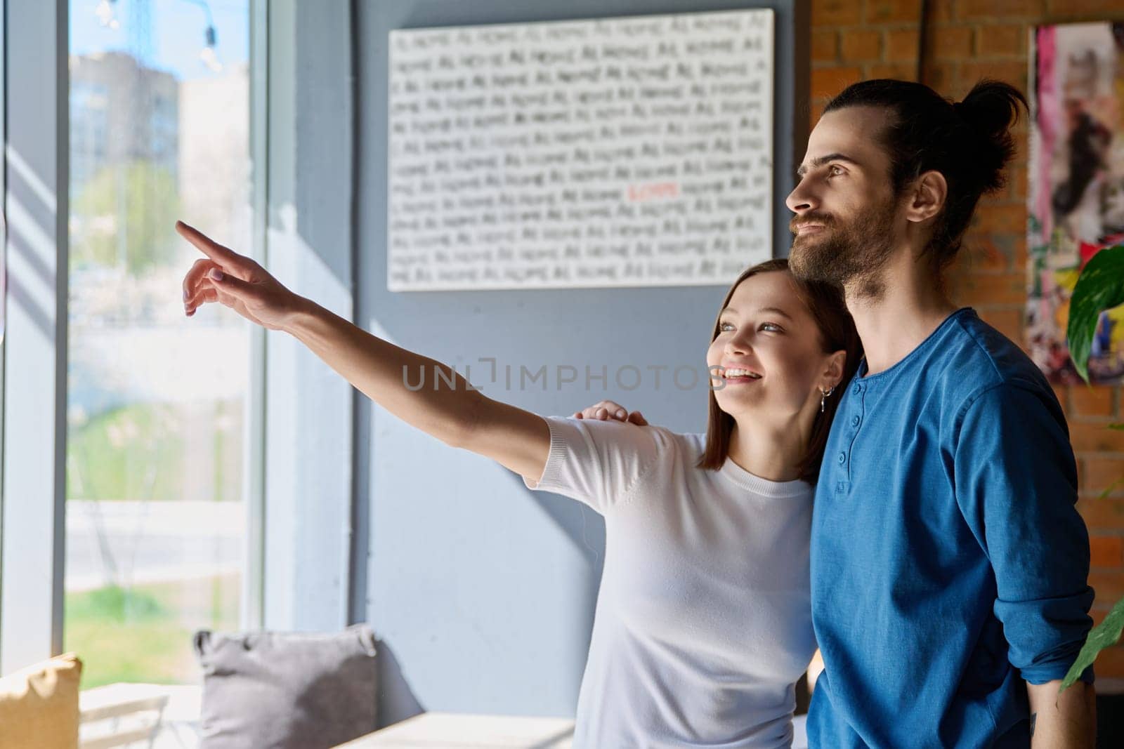 Young happy couple hugging together looking out the window. Love, friendship, romance, relationship, happiness, lifestyle, people concept