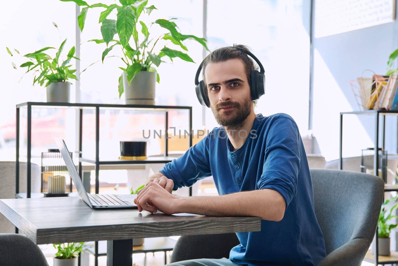 Portrait of young handsome man with headphones working with laptop, looking at camera by VH-studio