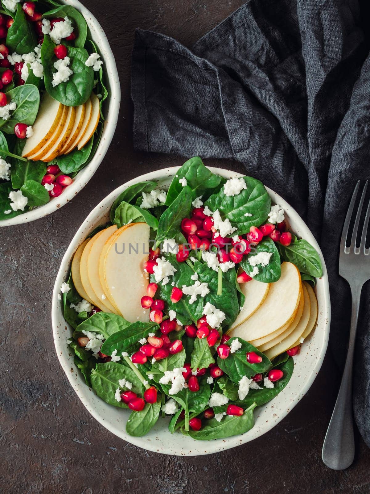 Vegan salad bowl with spinach, pear, pomegranate, cheese on black background. Vegan breakfast, vegetarian food, diet concept. Vertical. Top view or flat lay.