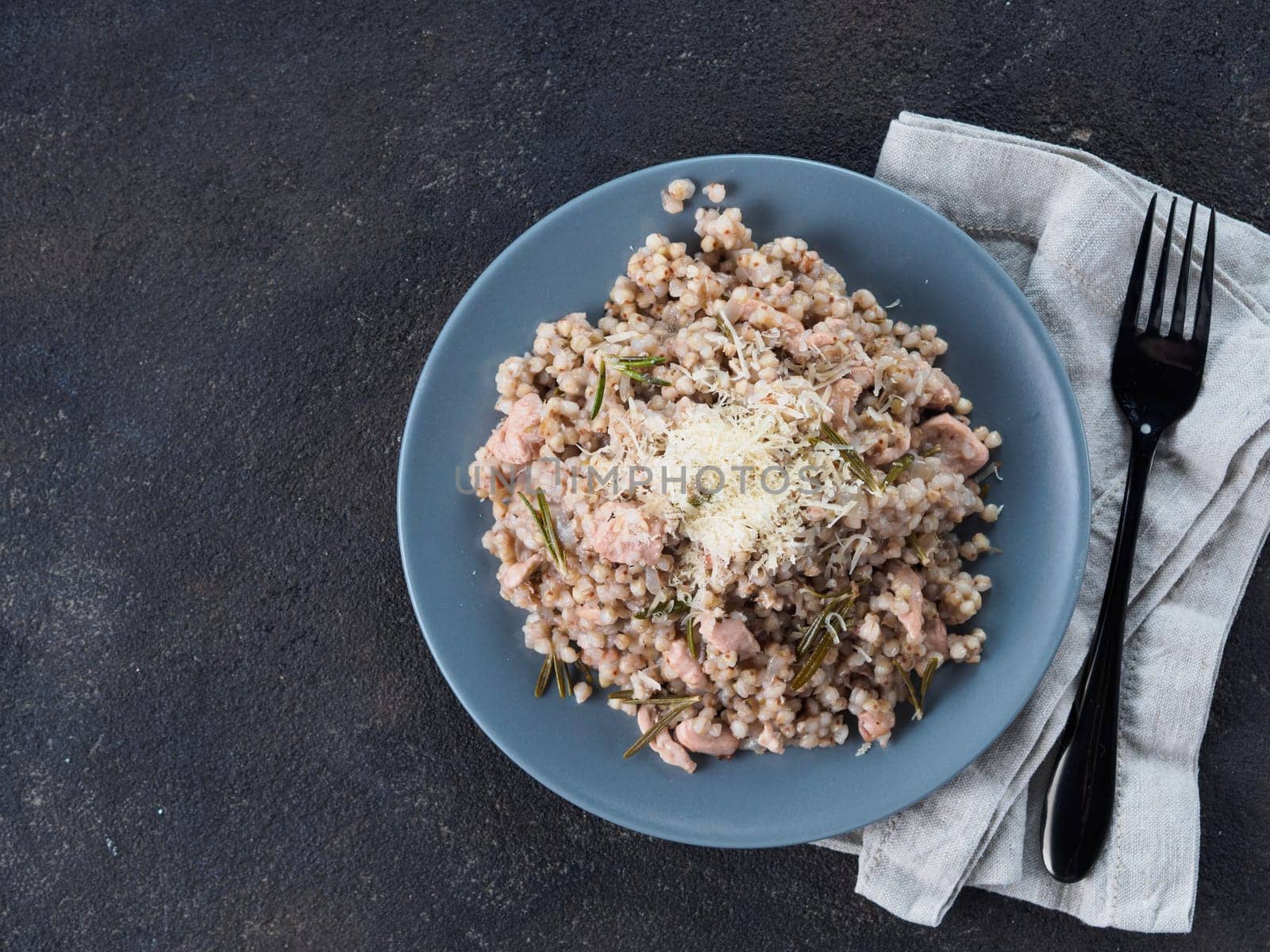 Raw buckwheat risotto with chicken meat and rosemary served parmesan cheese in gray plate on black cement background. Gluten-free and buckwheat recipe ideas. Copy space