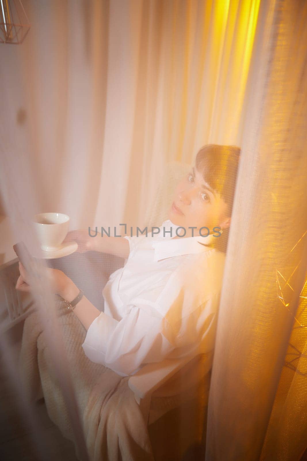 Nice girl with a mug of tea or coffee in cozy room. A middle-aged adult woman relaxing in the evening in the living room or bedroom in the evening