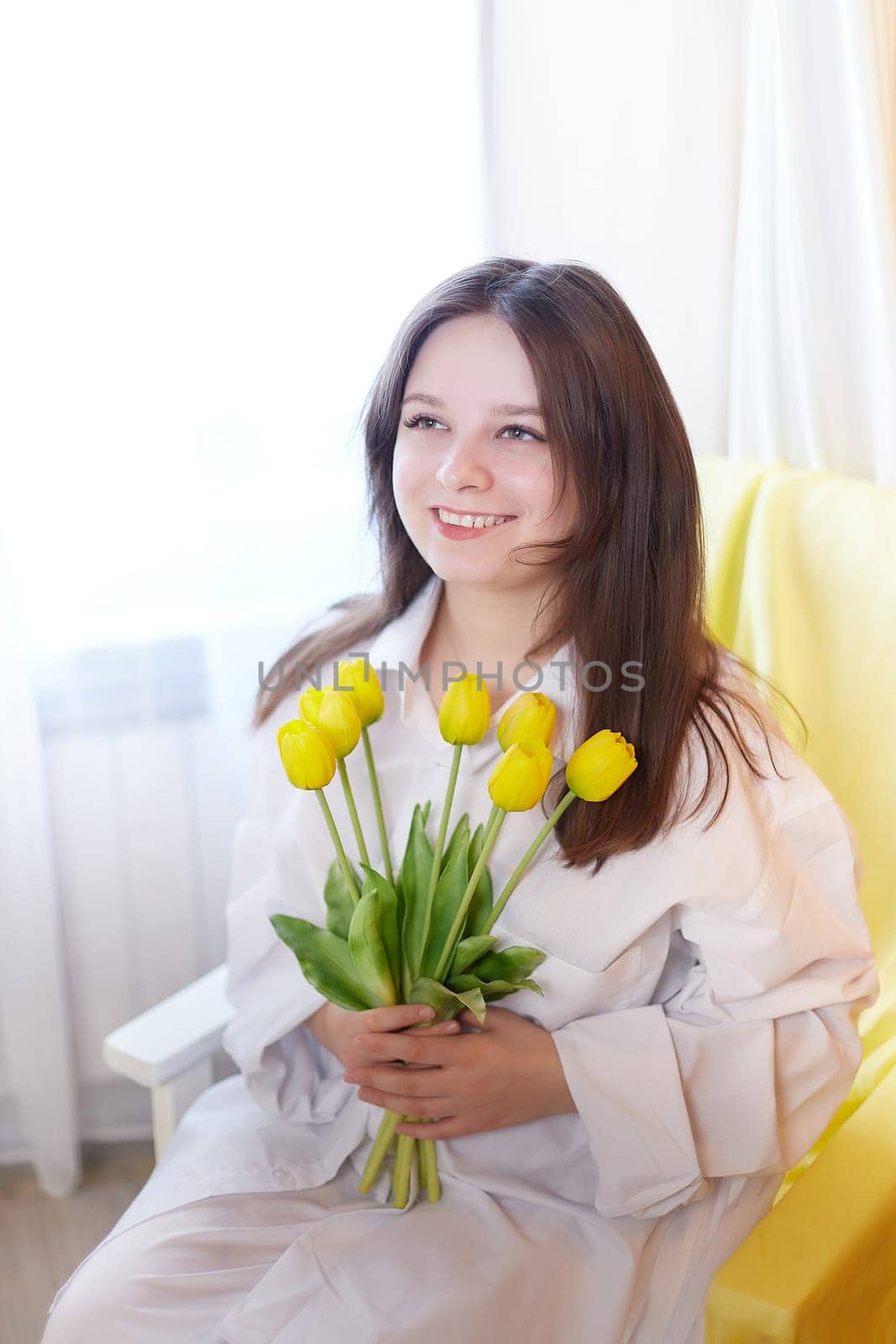 Beautiful sweet girl in nightgown in early morning with bouquet of delicate yellow tulips. Gift on International Women's Day on March 8th. Cosmetics, skin and hair care. Perfume, natural fragrance