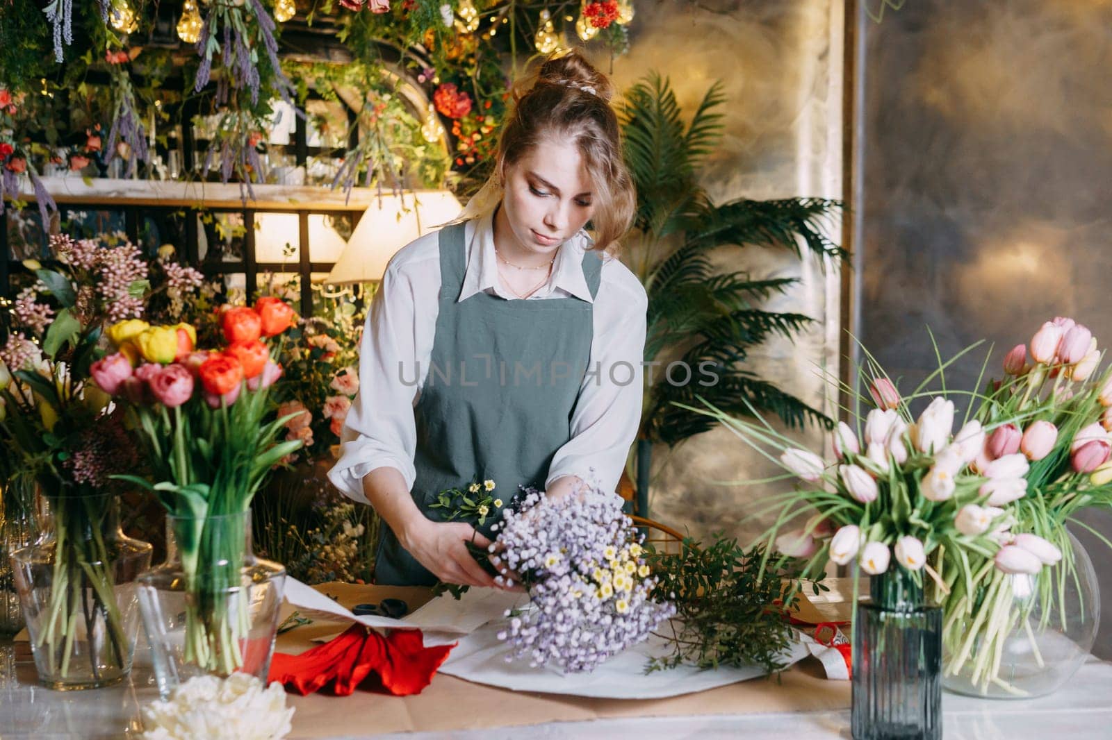 A woman in her florist shop collects bouquets of flowers. The concept of a small business. Bouquets of tulips for the holiday on March 8. by Annu1tochka