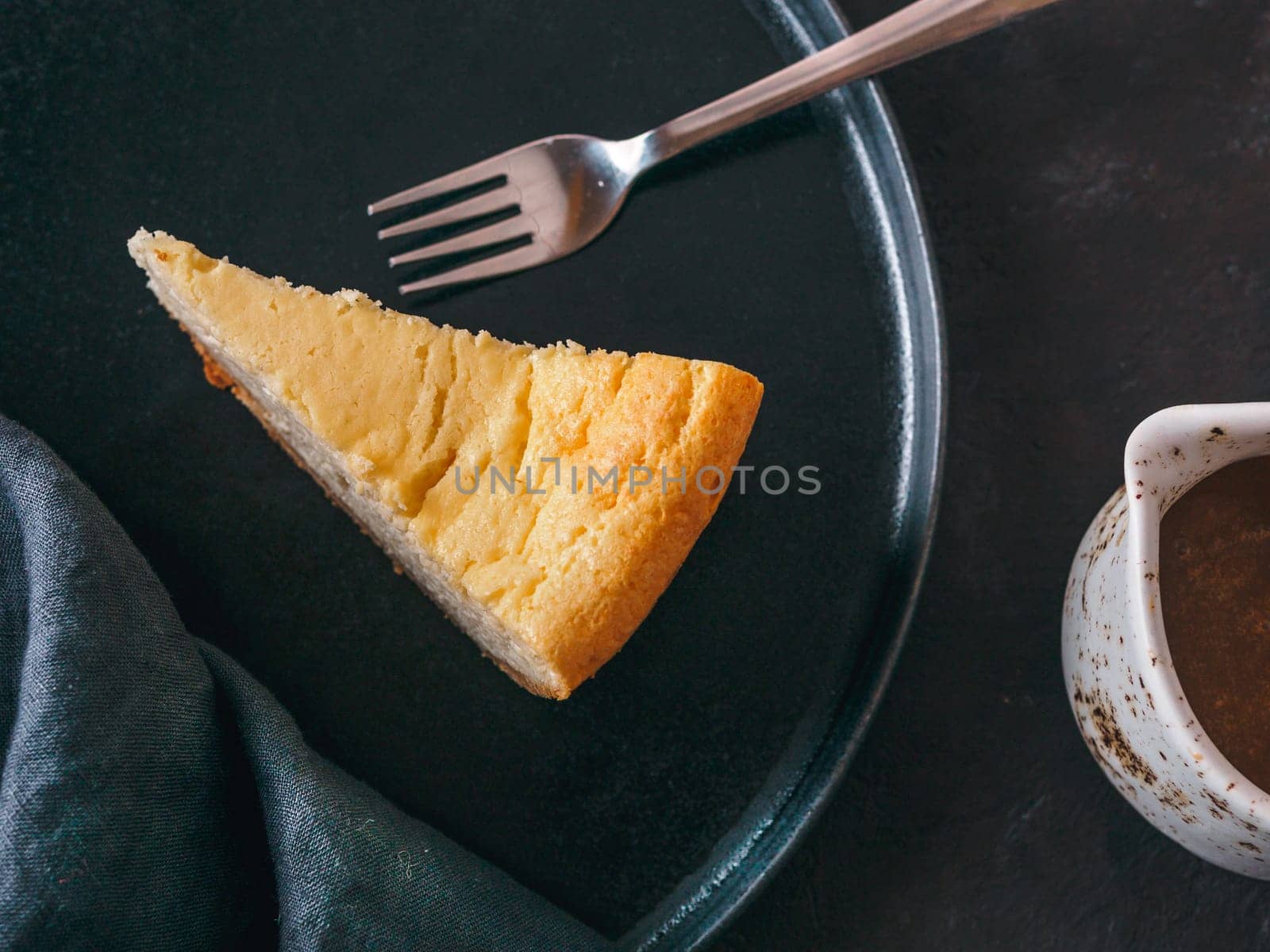 Plate with piece of cheesecake on dark background. Classic cheesecake, caramel sauce and dessert forks. Top view or flat lay.