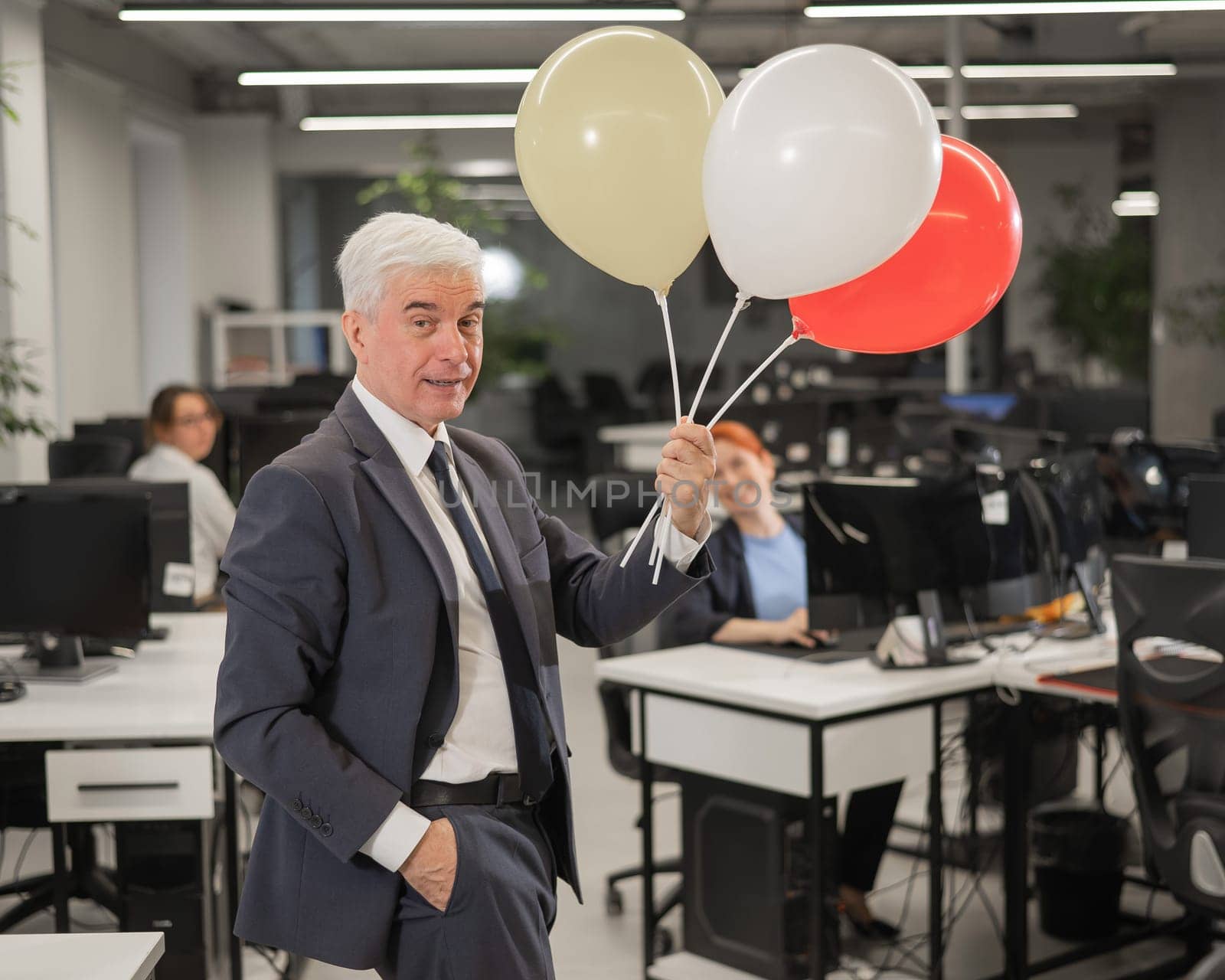 Portrait of a cheerful mature business man holding balloons in the office. by mrwed54