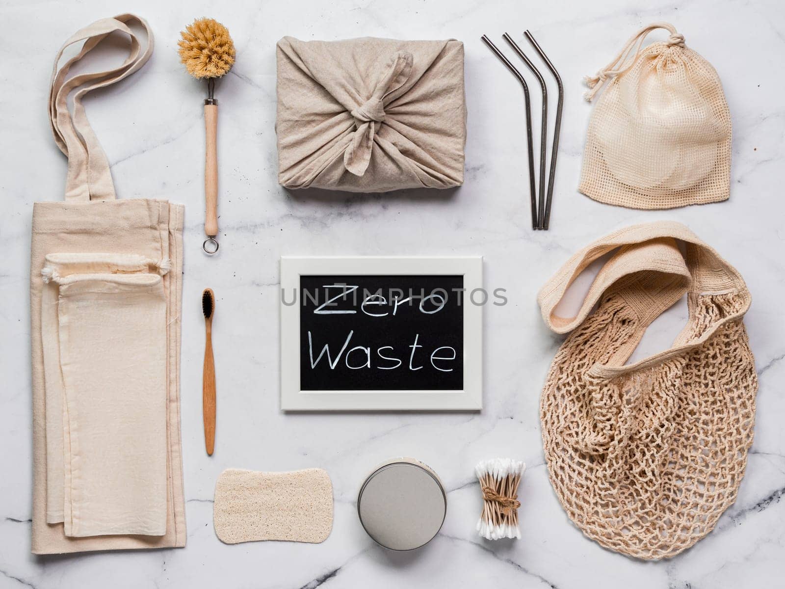 Zero waste concept. Textile wrapping gift, eco bags, metal straws, eco-friendly kitchen tools, bamboo toothbrush and cotton buds, reusable cotton pads on white marble background. Top view or flat lay