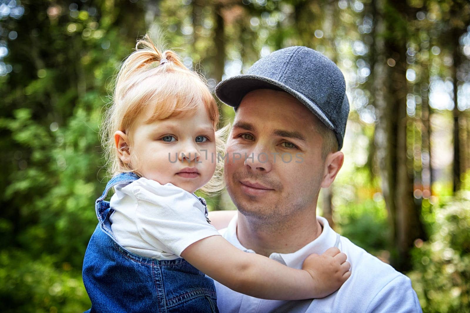 Gentle Father Holding Young Daughter Outdoors in Daylight. A tender moment as dad embraces his little girl in a sunny garden