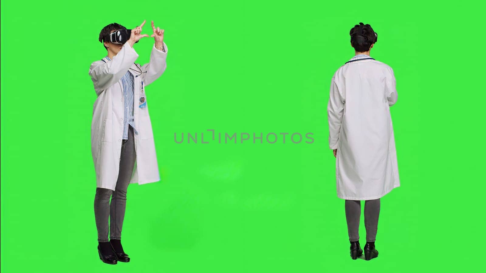 Woman medic works with 3d virtual reality headset in studio, standing against greenscreen backdrop. General practitioner uses vr glasses with interactive vision tool, futuristic exam. Camera A.