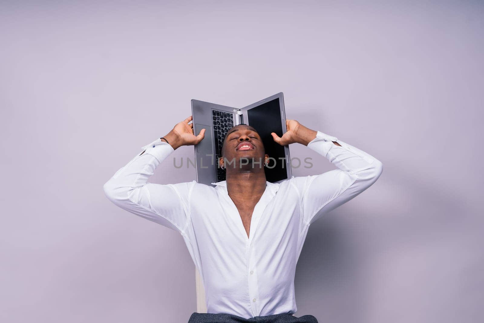 A man in a white Tshirt holds a laptop over his head with one hand by Zelenin
