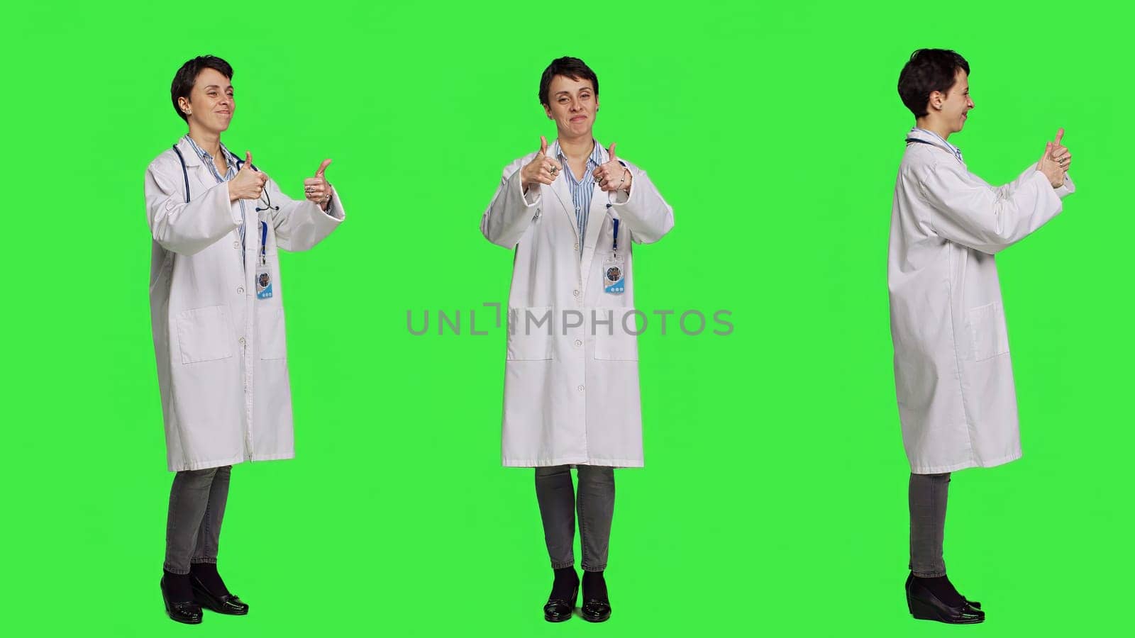 Cheerful medic doing thumbs up symbol against greenscreen backdrop, expresses positivity with like sign. General practitioner with coat giving approval and being satisfied with success. Camera B.