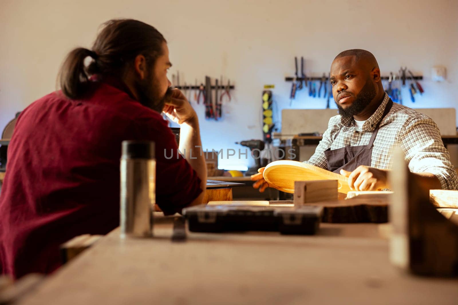 Manufacturer and apprentice discussing in studio to select best wood materials for project. Cabinetmaker and colleague talking in joinery, doing quality assurance on lumber piece