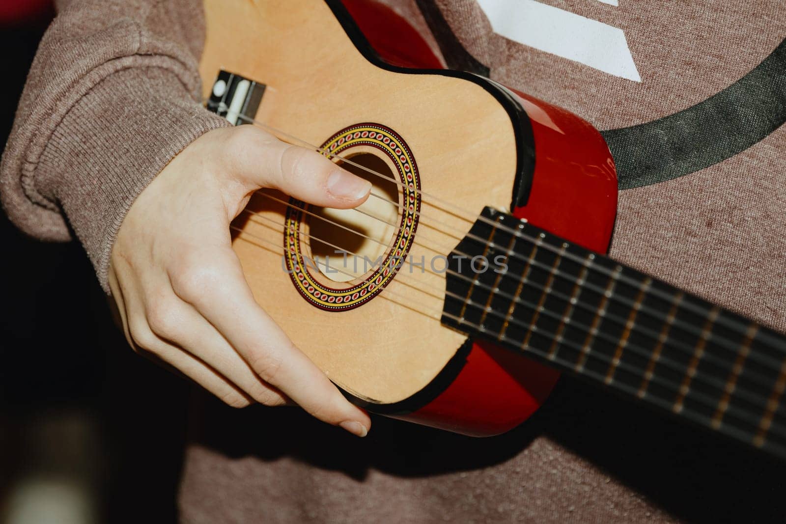 One unrecognizable teenage girl plucks the strings of a guitar with her fingers, close-up side view.