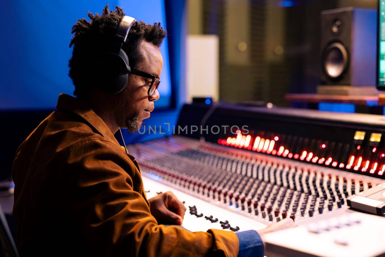 African american audio expert editing tracks in professional recording studio, mixing and mastering music in control room with technical gear. Sound engineer producing new tracks for an album.