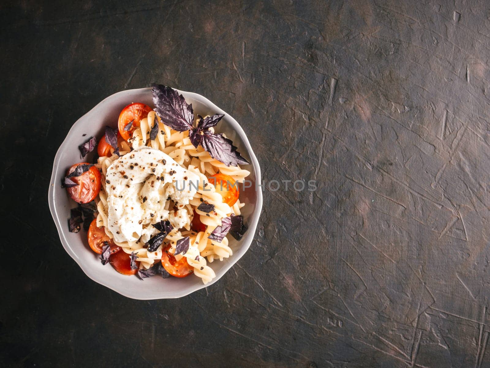Tasty italian fusilli pasta with cherry, mozarella or buratta cheese and fresh basil. Dish with pasta on black concrete background. Top view. Copy space. Healthy food concept and recipe idea.