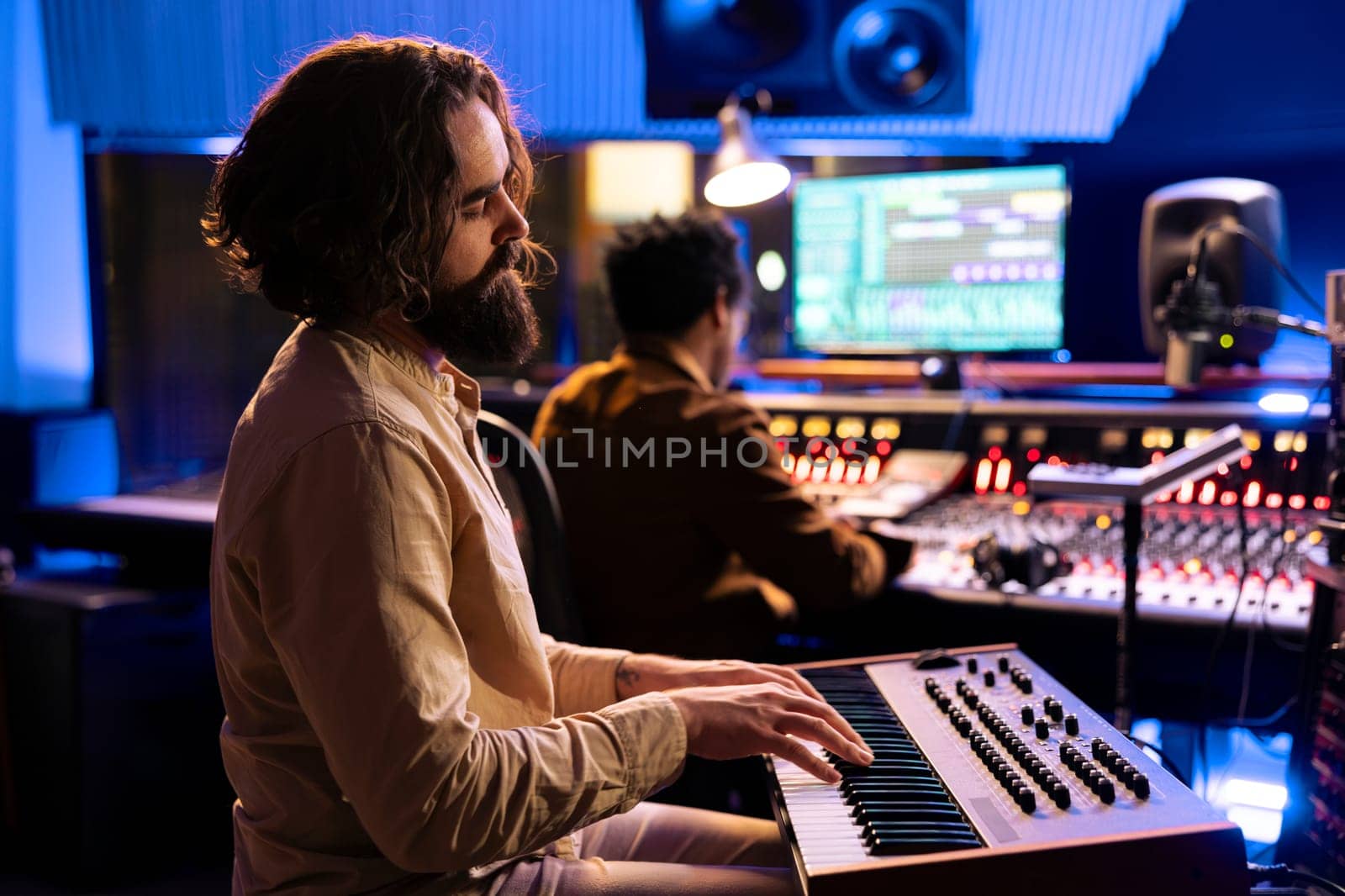 Young artist songwriter creating a new song with piano keys in studio, collaborating with audio engineer in control room. Musician singer composing music with midi controller electronic keyboard.