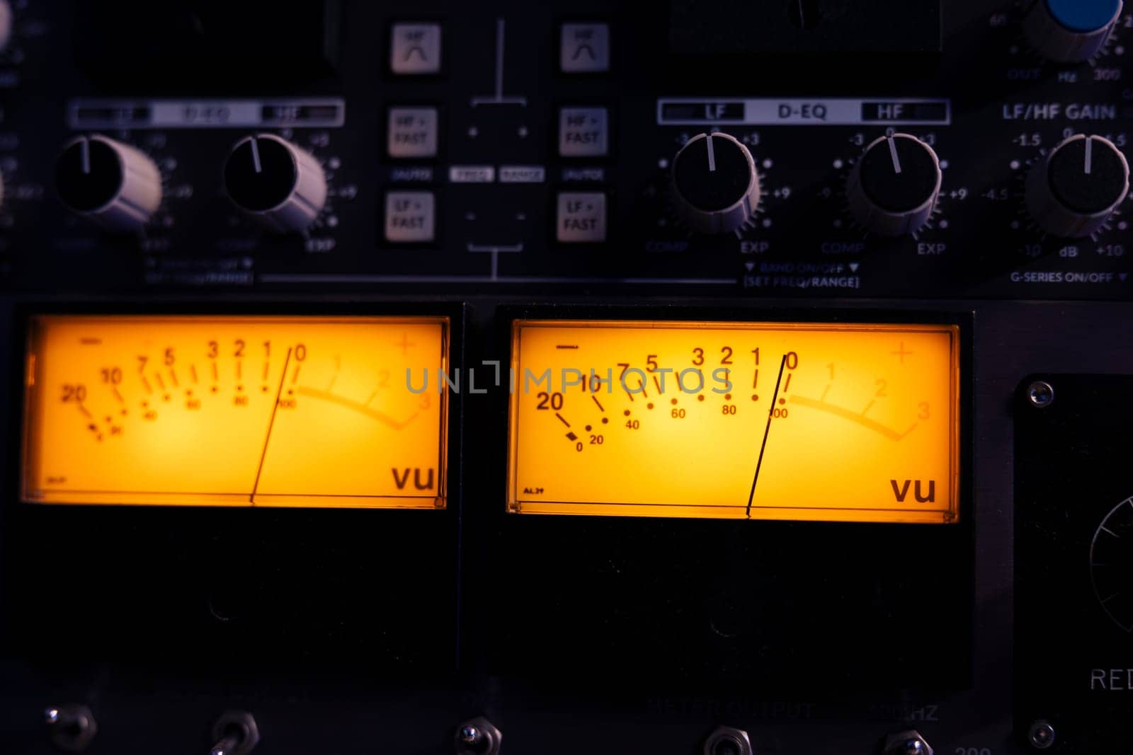 Technical recording equipment and devices for calibrating volume levels and sound settings in professional studio control room, yellow light. Audio mixer desk with switchers and sliders. Close up.