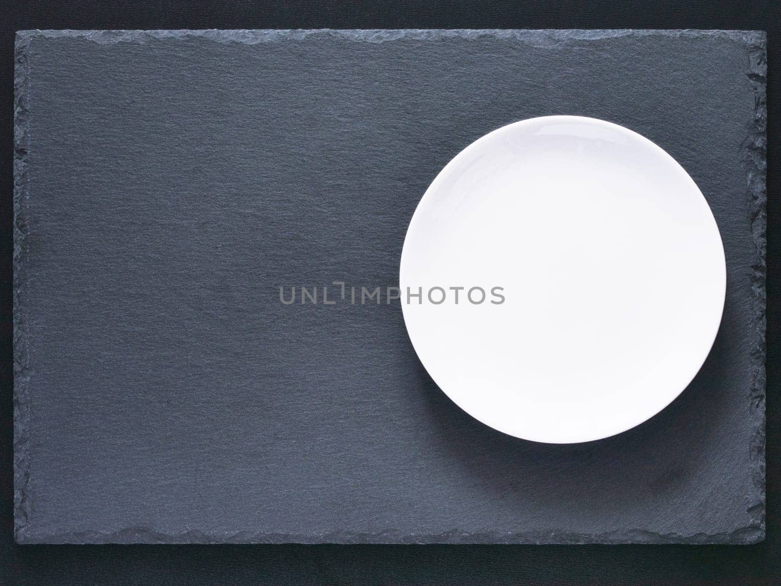 Empty white plate on black slate board on dark background. Flat lay or top view. Can use fo design menu