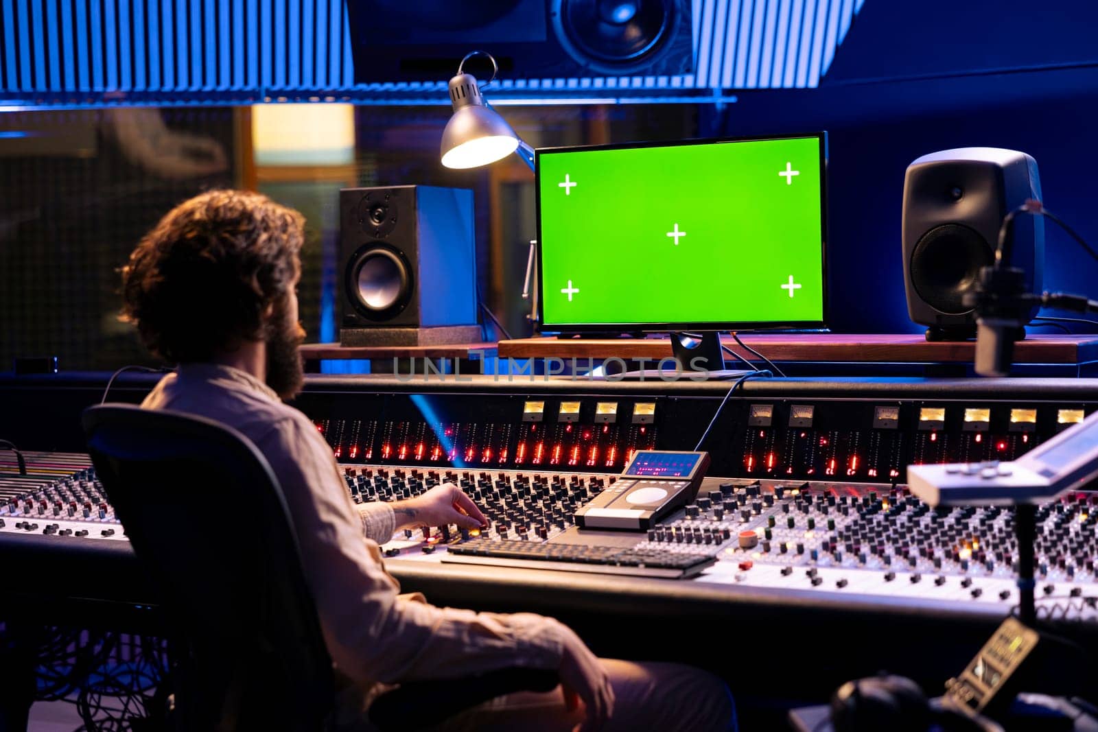 Sound designer working on mixing and mastering tracks with mockup display, using control panel board in professional studio. Skilled producer looks at greenscreen, editing music.
