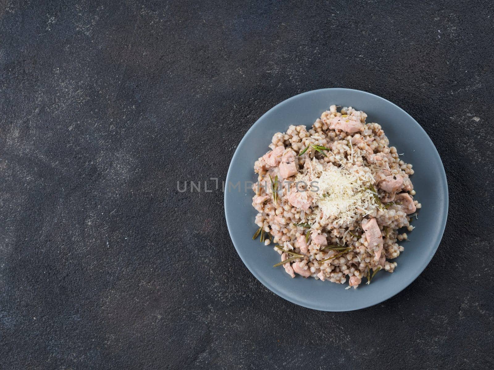 Raw buckwheat risotto with chicken meat and rosemary served parmesan cheese in gray plate on black cement background. Gluten-free and buckwheat recipe ideas. Copy space.