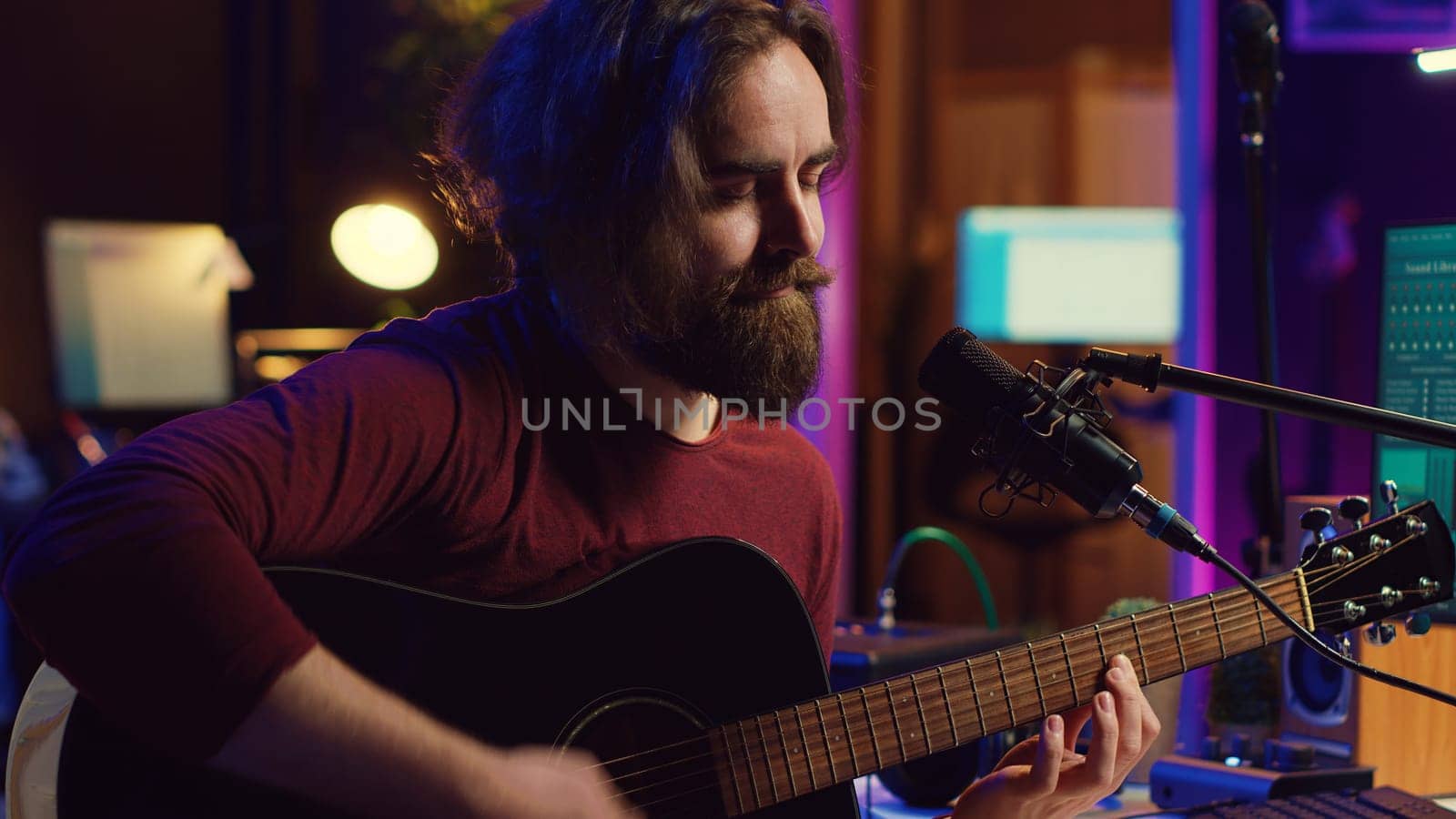 Artist with condenser microphone composing a song on guitar, working on mixing and mastering music. Producer recording tunes and adding sound effects in post production. Camera A.