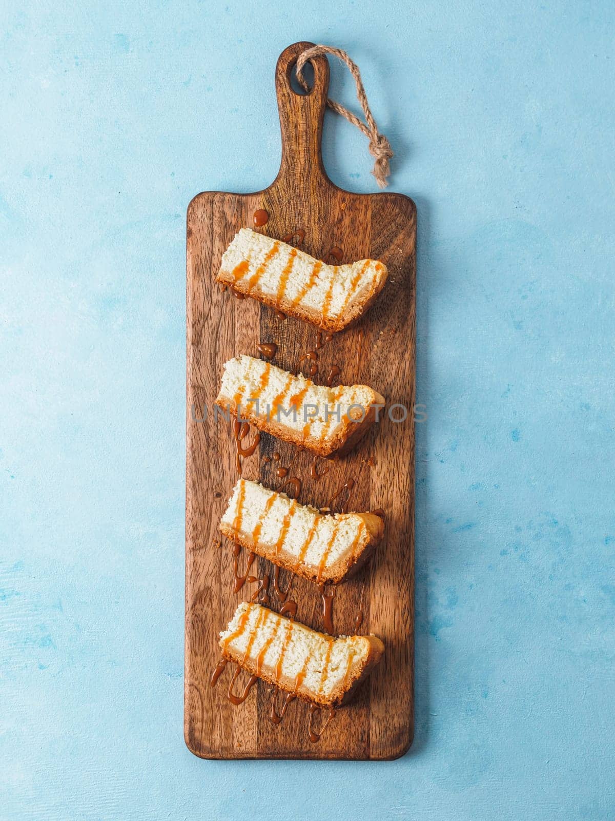 caramelized cheesecake slices on wooden cuttingboard. Cheesecake on blue background with copy space for text. Top view or flat lay. Vertical.