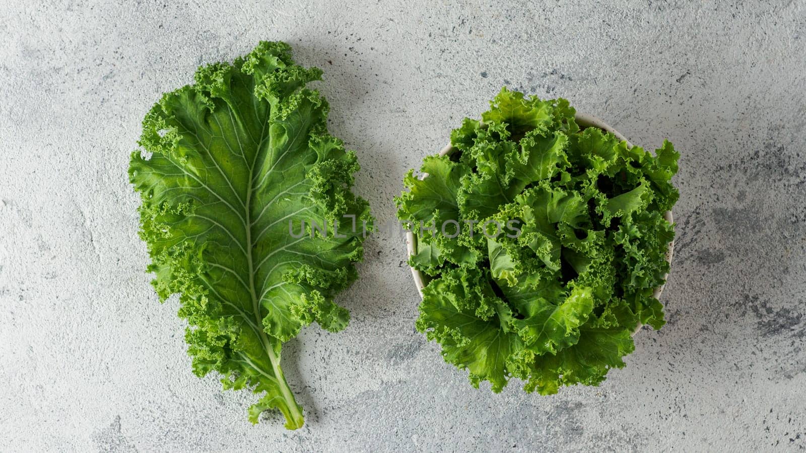 Fresh green kale leaf and salad on gray cement background, top view. Healthy detox vegetables. Clean eating and dieting concept. Flat lay. Health kale benefits