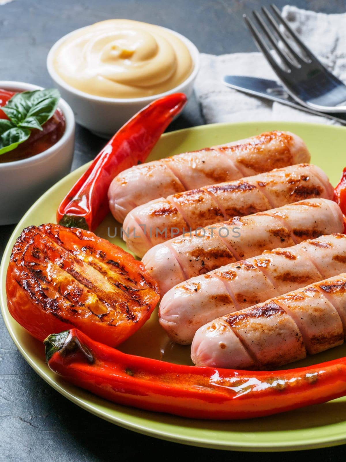 Close up view of chicken homemade sausages with sauces ketchup and mustard. Grilled sausages and grilled vegetables in green plate. Copy space. Vertical.