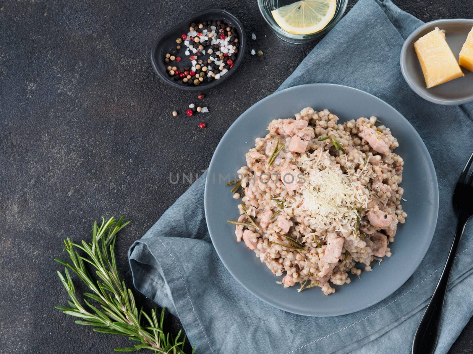 Raw buckwheat risotto with chicken meat and rosemary served parmesan cheese in gray plate on black cement background. Gluten-free and buckwheat recipe ideas. Copy space. Top view or flat-lay.