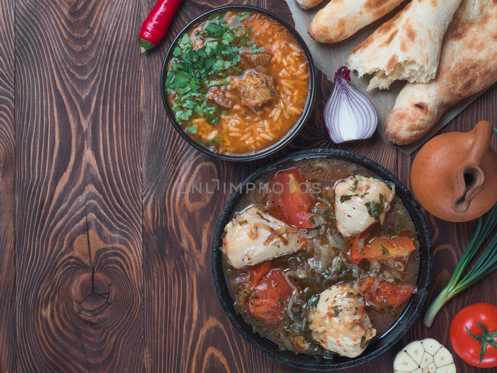 Traditional Georgian kitchen - spicy Kharcho soup and chicken Chachochbili, traditional bread Shotis Puri, vintage wine jar, fresh vegetables on wooden table. Copy space for text. Top view
