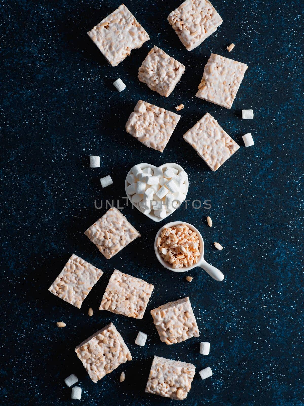 Homemade square bars of Marshmallow and crispy rice and ingredients on dark blue background. American dessert with marshmallow and crispy rice. Top view. Copy space