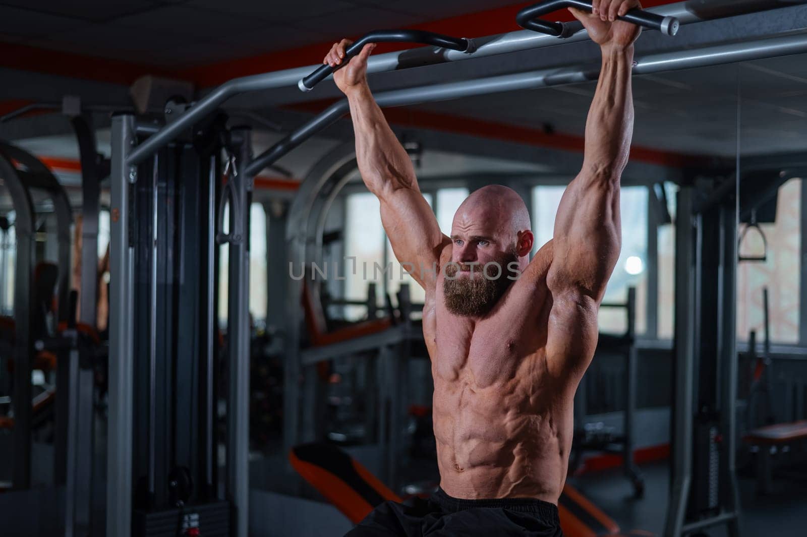 Caucasian man hangs on the horizontal bar and raises his legs