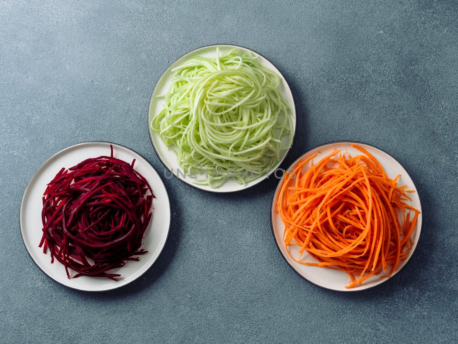 Vegetable noodles - zucchini, carrot, and beetroot noodles on plate over gray stone background. Clean eating, raw vegetarian, food concept. Copy space for text. Top view or flat lay.