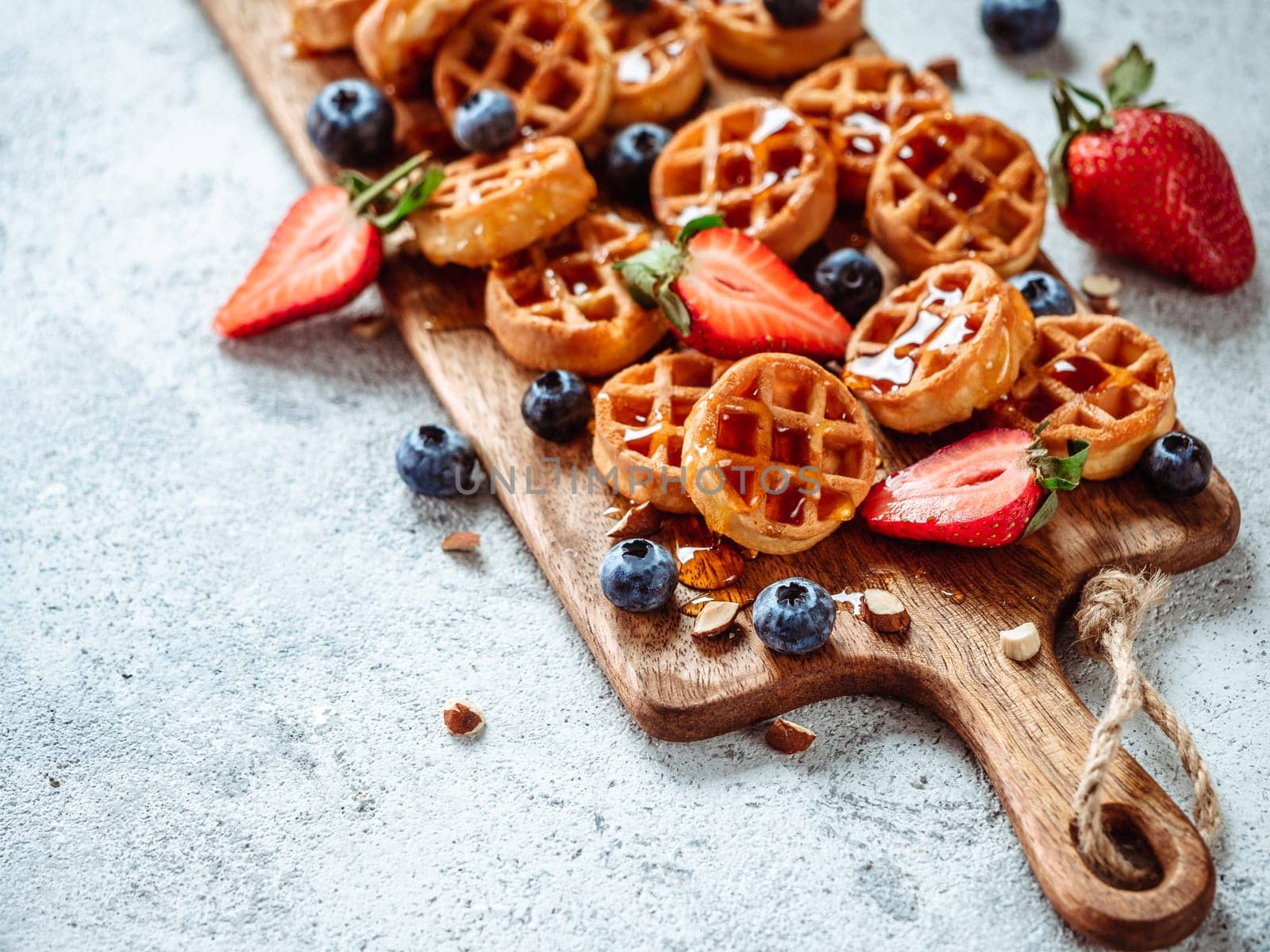 Small round delicious soft belgian waffles on cutting board. Fresh belgian waffles with berries and caramel sauce top view. Copy space for text or mock up