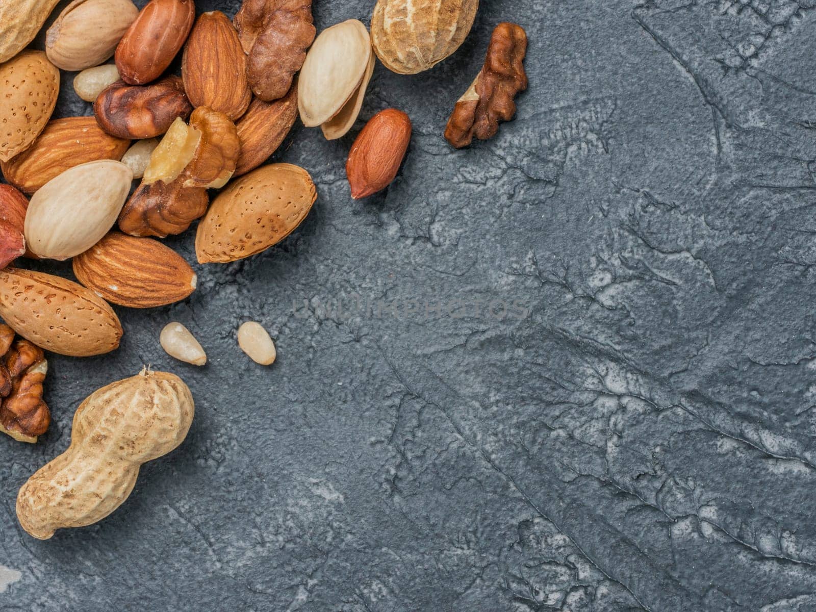 Background of mixed nuts - hazelnuts, walnuts, almonds - on dark concrete background with copy space. Top view or flat lay